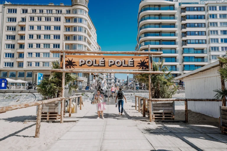 Boardwalk entrance to the beach bar under a Polé Polé sign, seen from the sand with seafront apartment blocks behind