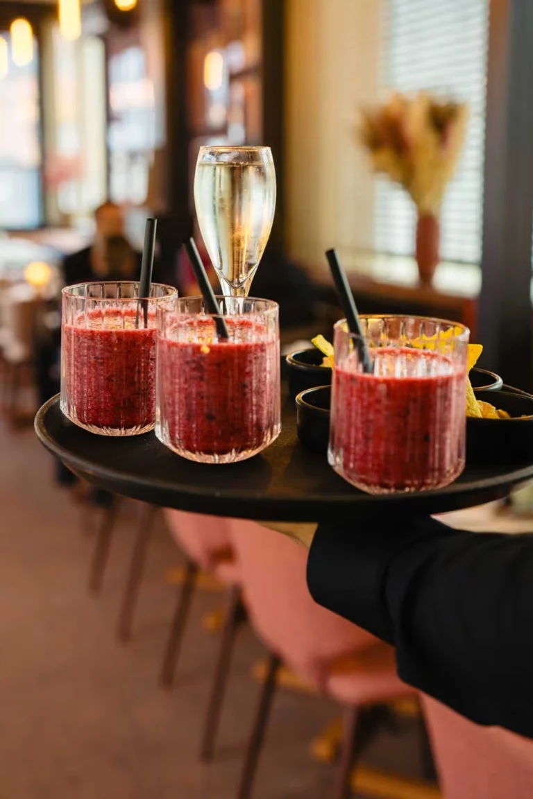 Waiter carrying a tray of three berry smoothies and a glass of sparkling wine through the dining room