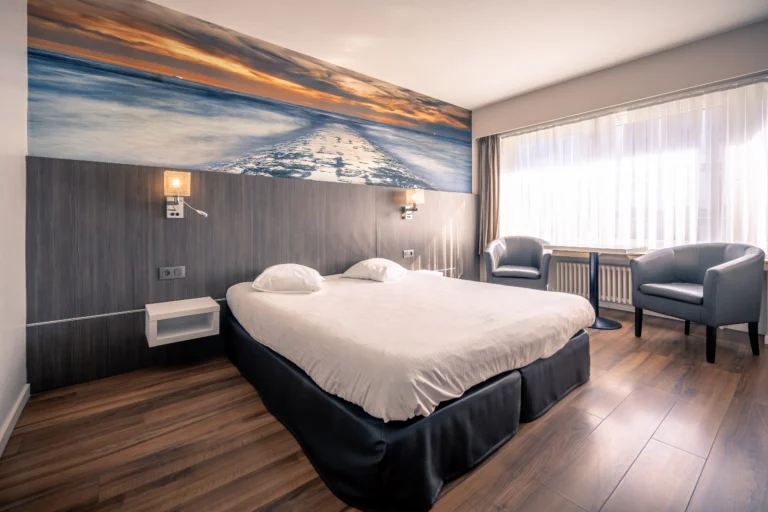 Hotel room with twin beds pushed together, two armchairs and a wide coastal photo mural behind the bed
