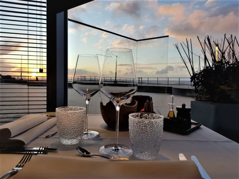 Table set with wine glasses in a glass corner window, the sun setting over the promenade and sea