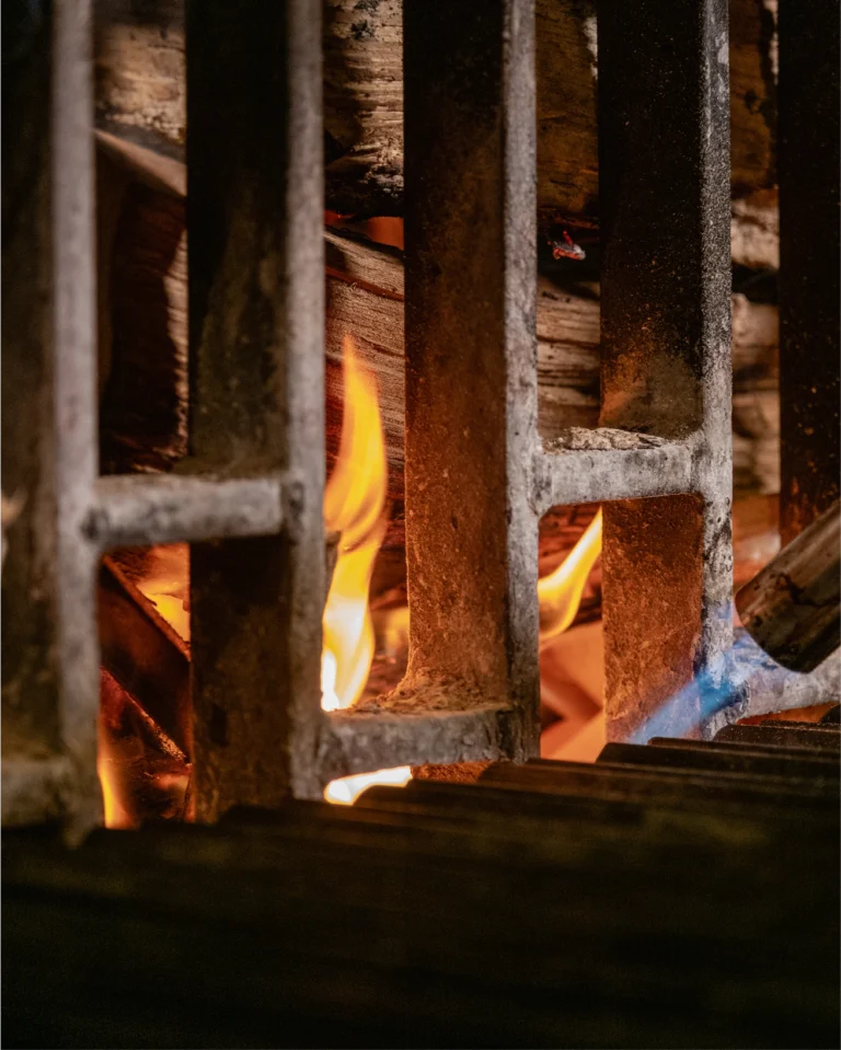Flames burning beneath the bars of a charcoal grill