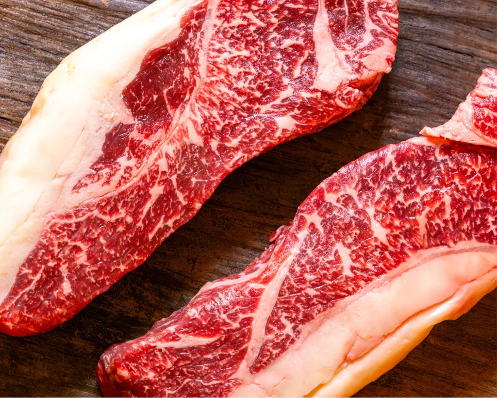 Two thick, well-marbled raw beef steaks on a wooden board