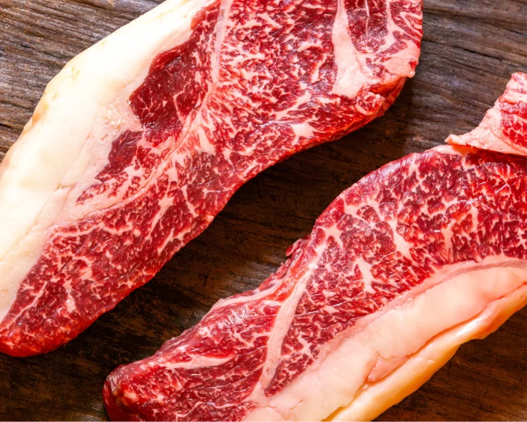 Two thick, well-marbled raw beef steaks on a wooden board