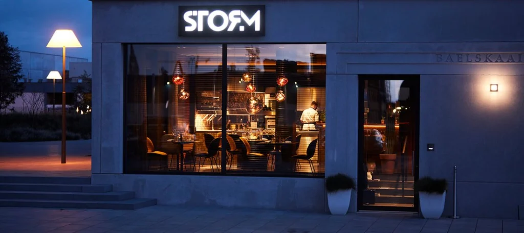 STORM's glass frontage at dusk, with the lit dining room visible beneath the restaurant's sign