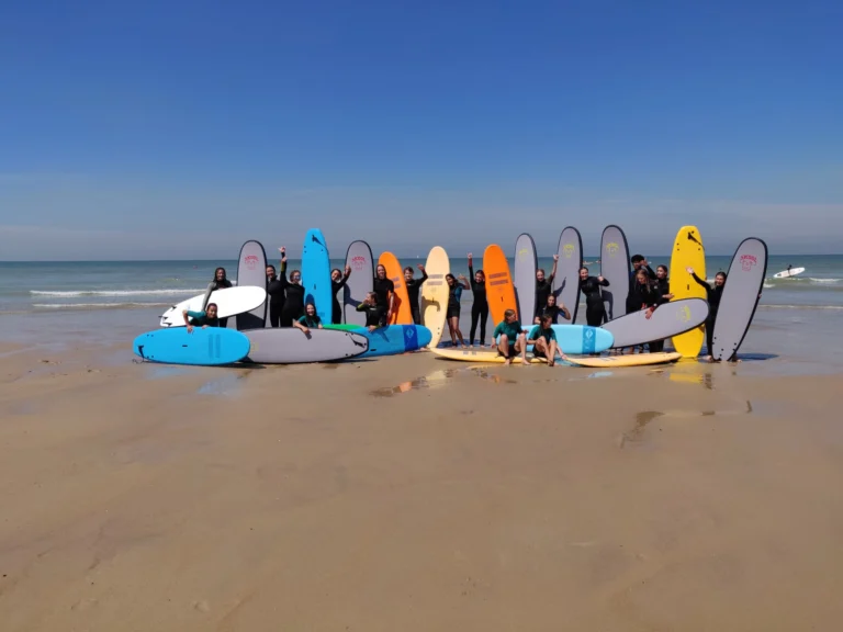 Surf camp group in wetsuits with a row of colourful surfboards at the water's edge
