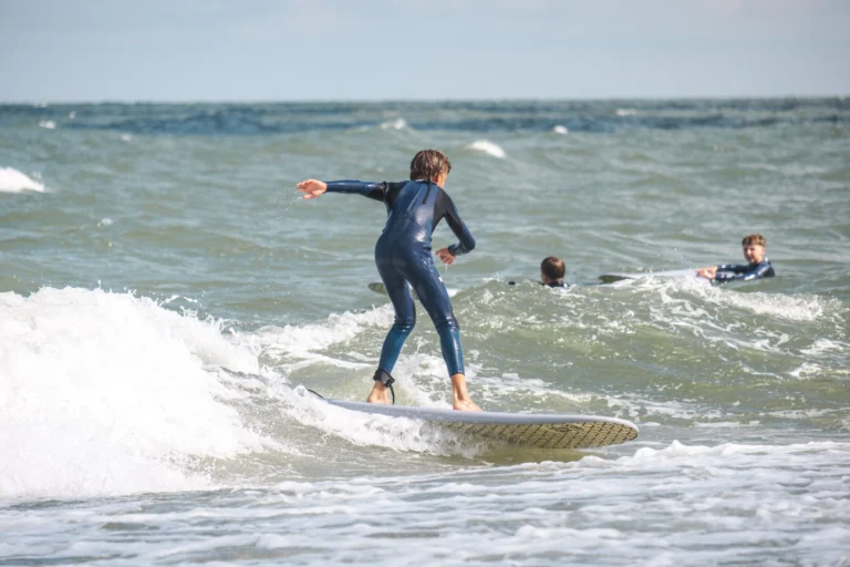 Young surfer balancing on a board in breaking surf while others wait in the water