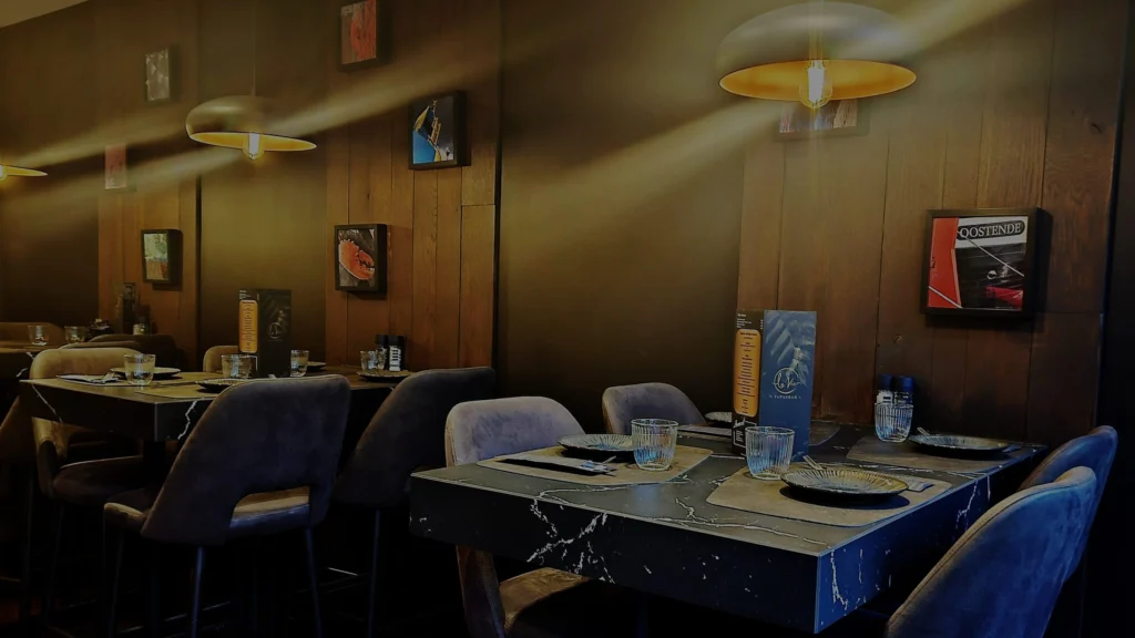 Dimly lit dining room at La Vie with wood-panelled walls, framed Ostend photographs, pendant lamps and laid tables with grey velvet chairs