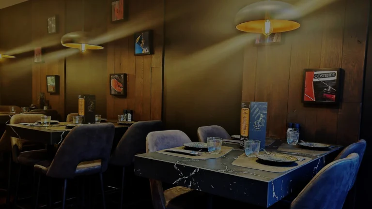 Dimly lit dining room at La Vie with wood-panelled walls, framed Ostend photographs, pendant lamps and laid tables with grey velvet chairs
