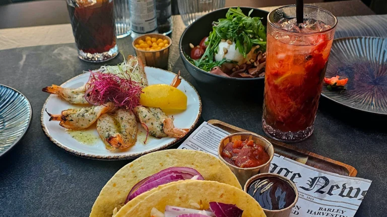 Table with grilled scampi, tacos with red onion, a burrata salad and a red fruit cocktail at La Vie