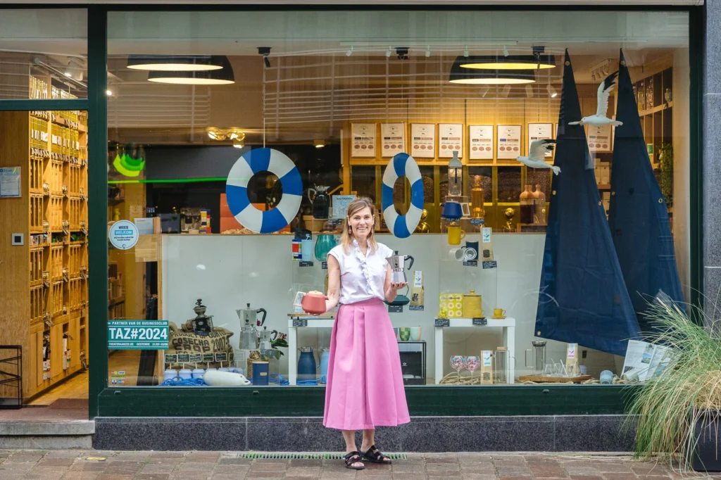 Tealicious shop window decorated with lifebuoys and navy sails, wooden tea shelves inside and a woman in a pink skirt standing in front