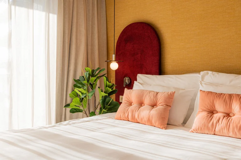 Double room with an arched red velvet headboard, peach cushions, warm wall lights and a leafy plant