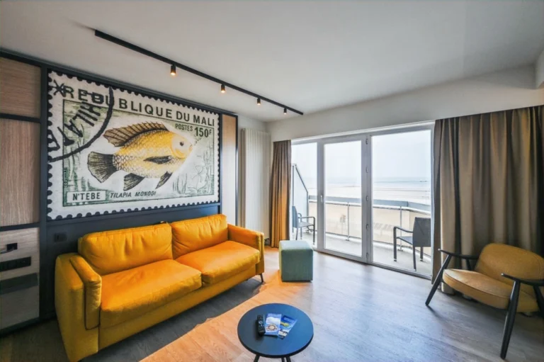 Room with a mustard-yellow sofa, a large stamp-style fish artwork and sliding doors to a balcony facing the sea