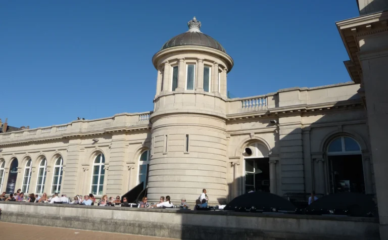 Round corner tower with a copper dome and arched windows above a sunny terrace on the promenade