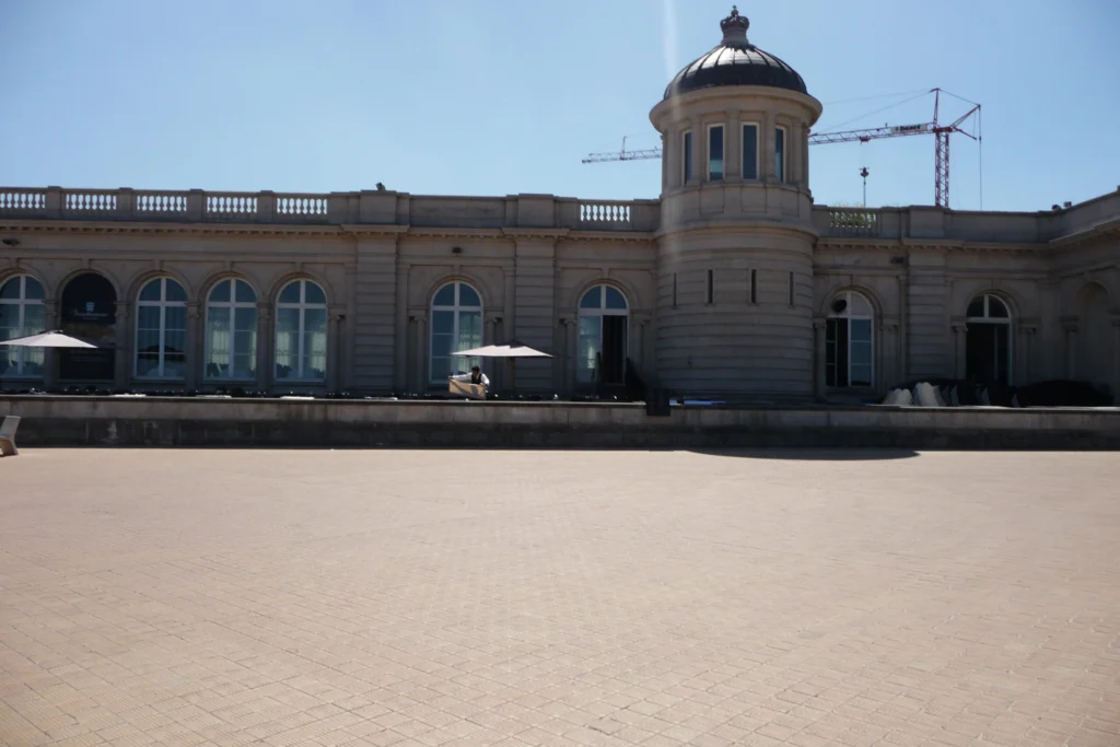 Long cream-coloured façade of the Venetian Galleries with arched windows and a domed corner tower, seen across an empty paved promenade