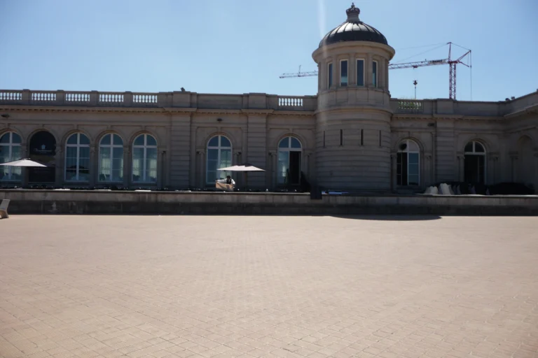 Long cream-coloured façade of the Venetian Galleries with arched windows and a domed corner tower, seen across an empty paved promenade