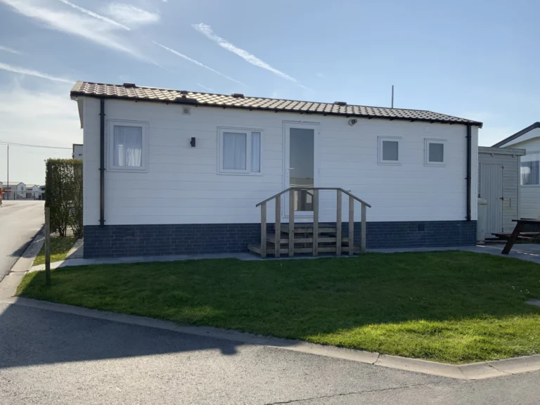 White mobile home with wooden entrance steps and a picnic table on a neat lawn