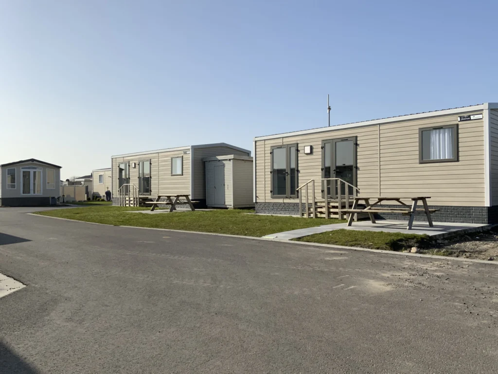Rows of modern mobile homes with picnic benches and lawns along a quiet park lane
