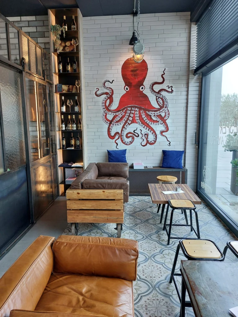 Lounge corner with leather sofas, tiled floor and a red octopus painted on a white brick wall, next to tall windows
