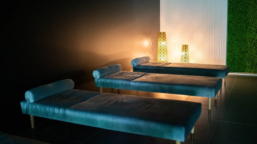 Three turquoise velvet loungers in a dimly lit relaxation room with warm lamps against a green plant wall