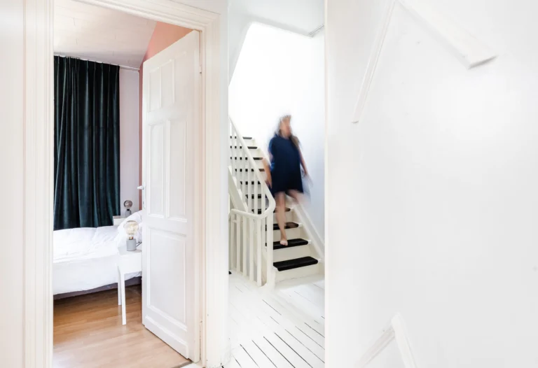 White hallway with a view into a bedroom and a black-and-white painted staircase