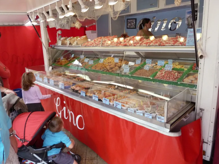 Seafood counter at a red fish stall on the Visserskaai with trays of shellfish, children looking in