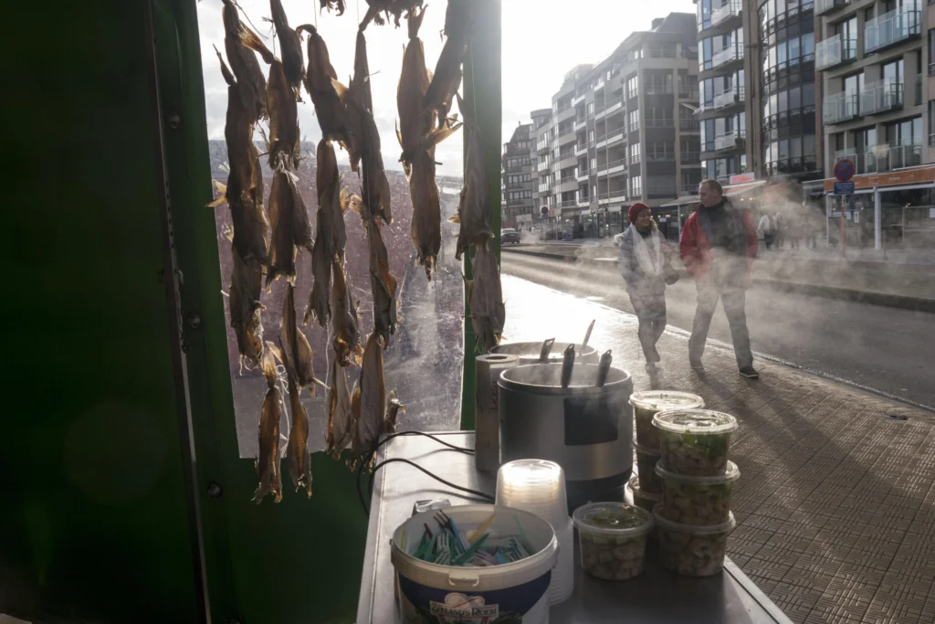 Seafood stall on the Visserskaai with dried fish hanging in the window and steaming pots of whelks, as people walk past in low winter sun