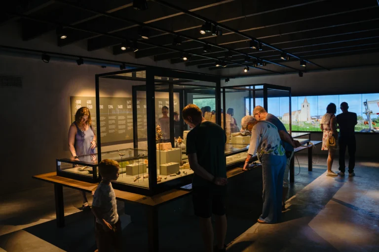 Visitors studying lit glass display cases of archaeological finds in the dark Walraversyde museum gallery