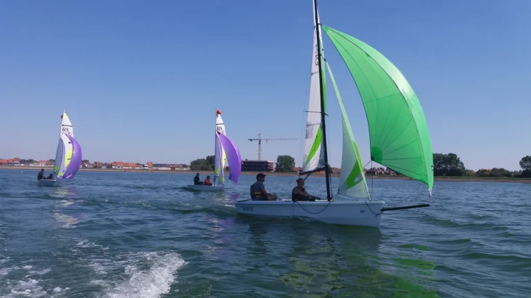 Two-person dinghy with a green spinnaker sailing on the Spuikom, other boats following