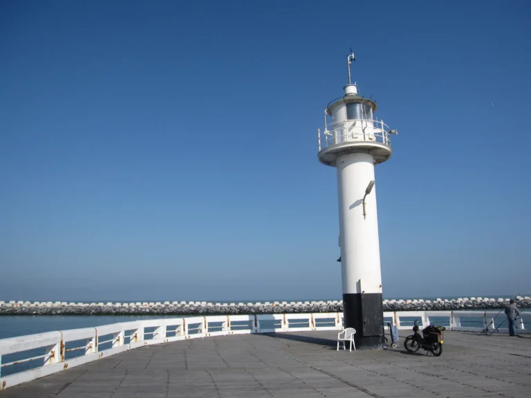 The white pier-head lighthouse with a black base at the end of the West Pier under a deep blue sky