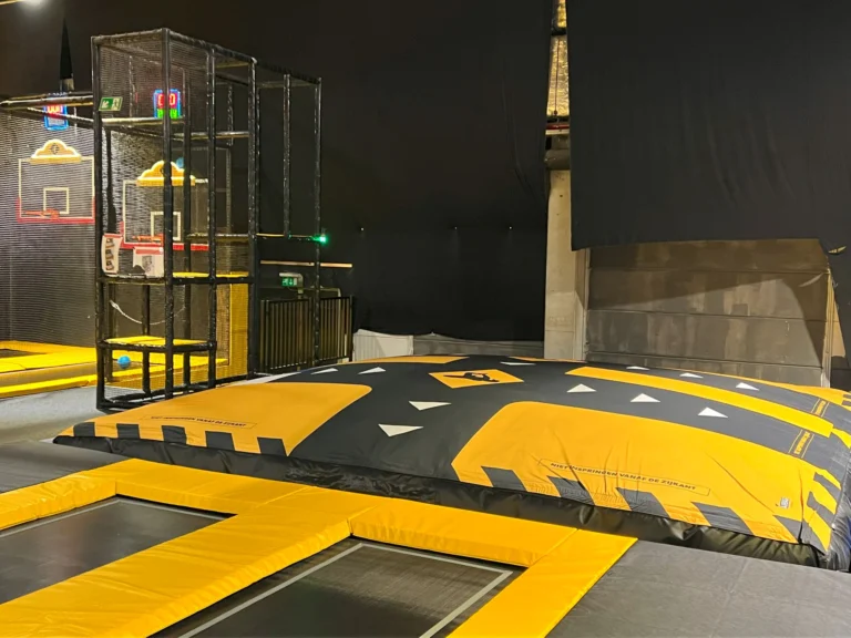 Large yellow and black airbag beside trampolines and netted slam-dunk basketball hoops