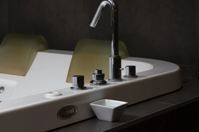 White jacuzzi bath with padded headrests and a chrome tap set into a dark surround